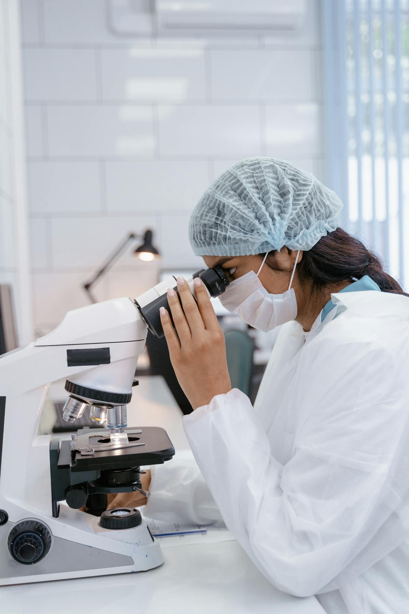 Female scientist in lab coat using microscope for research in a laboratory setting.